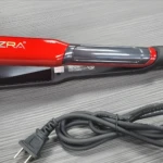 Plancha para cabello color rojo brillante marca Ezra con cable negro enroscado, sobre superficie texturizada gris.
