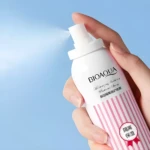 Spray protector solar Bioaqua blanco con líneas rosadas, rociando en mano femenina, ideal para hidratar y proteger.