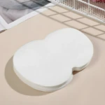 Pila de 10 parches protectores de sudor axilas blancos, forma contorneada, sobre superficie beige con sombras de rejilla.