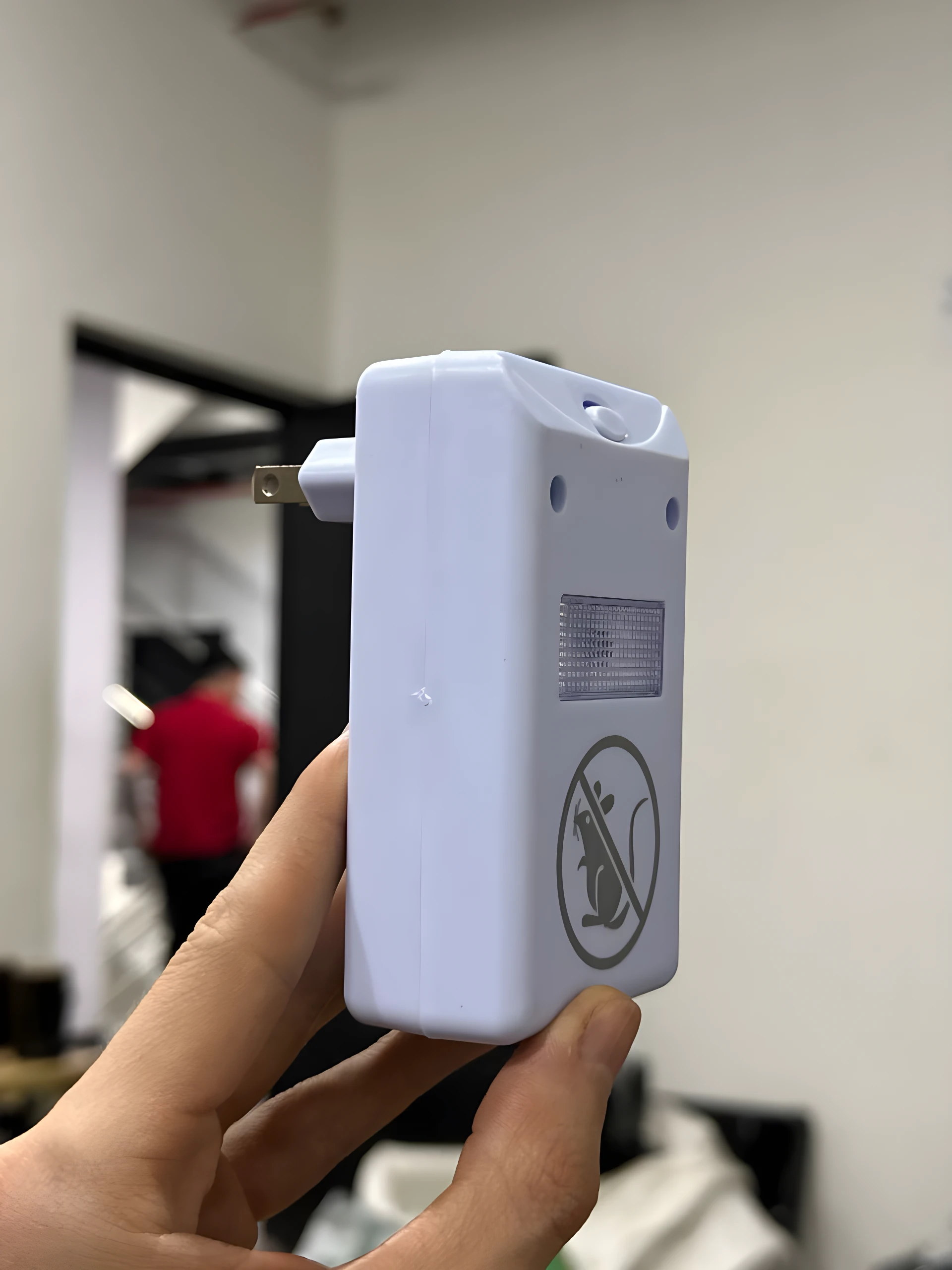 Repelente ultrasónico Ridex blanco, mostrado de cerca en mano, con símbolo de no ratones y enchufe visible.