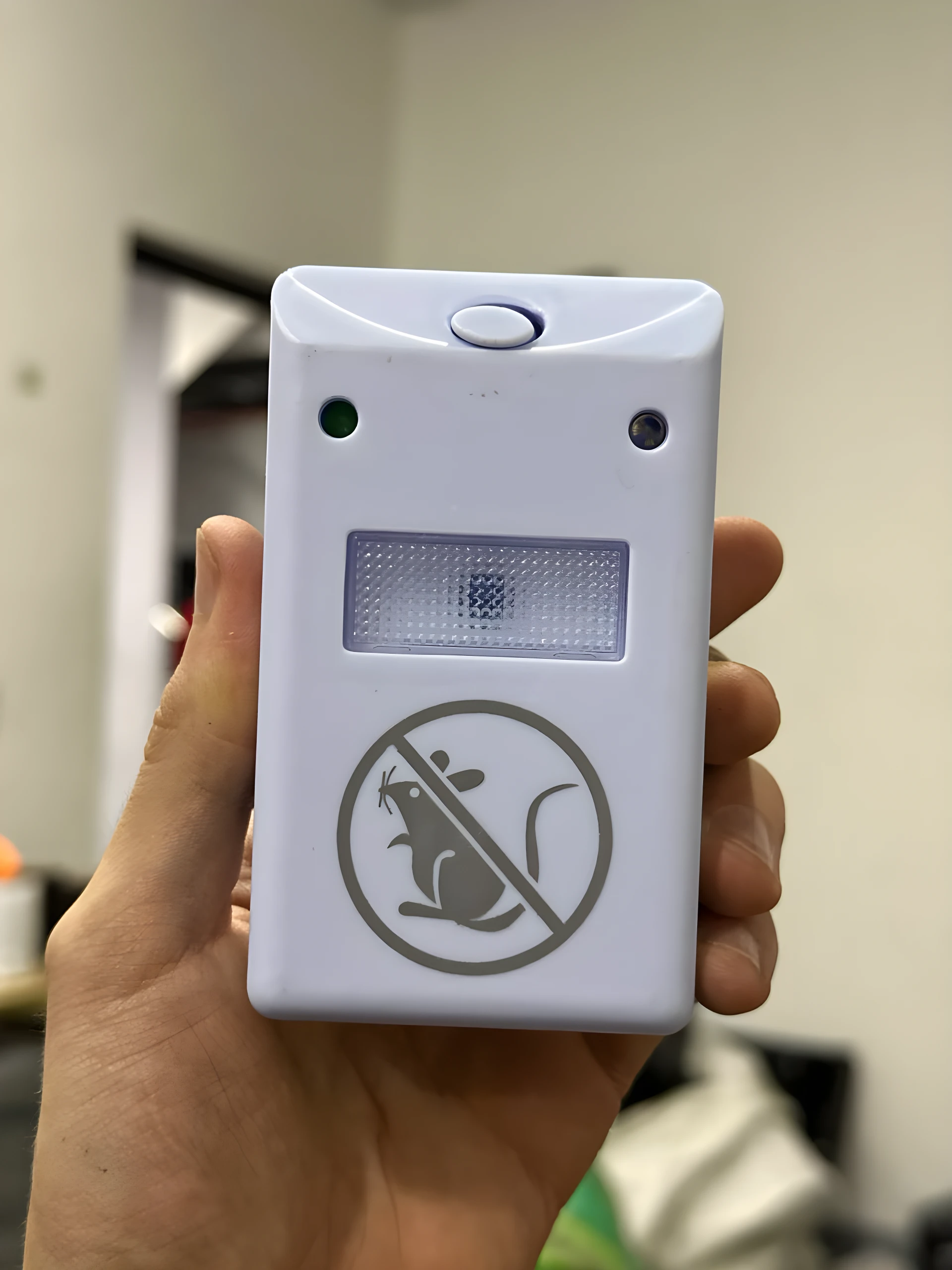 Repelente ultrasónico blanco Ridex en mano, mostrando botón superior, dos LEDs y pictograma de rata prohibida.