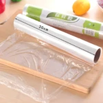 Rollo de película plástica transparente para alimentos, de 30cm de ancho, sobre una tabla de madera con un rollo adicional detrás.