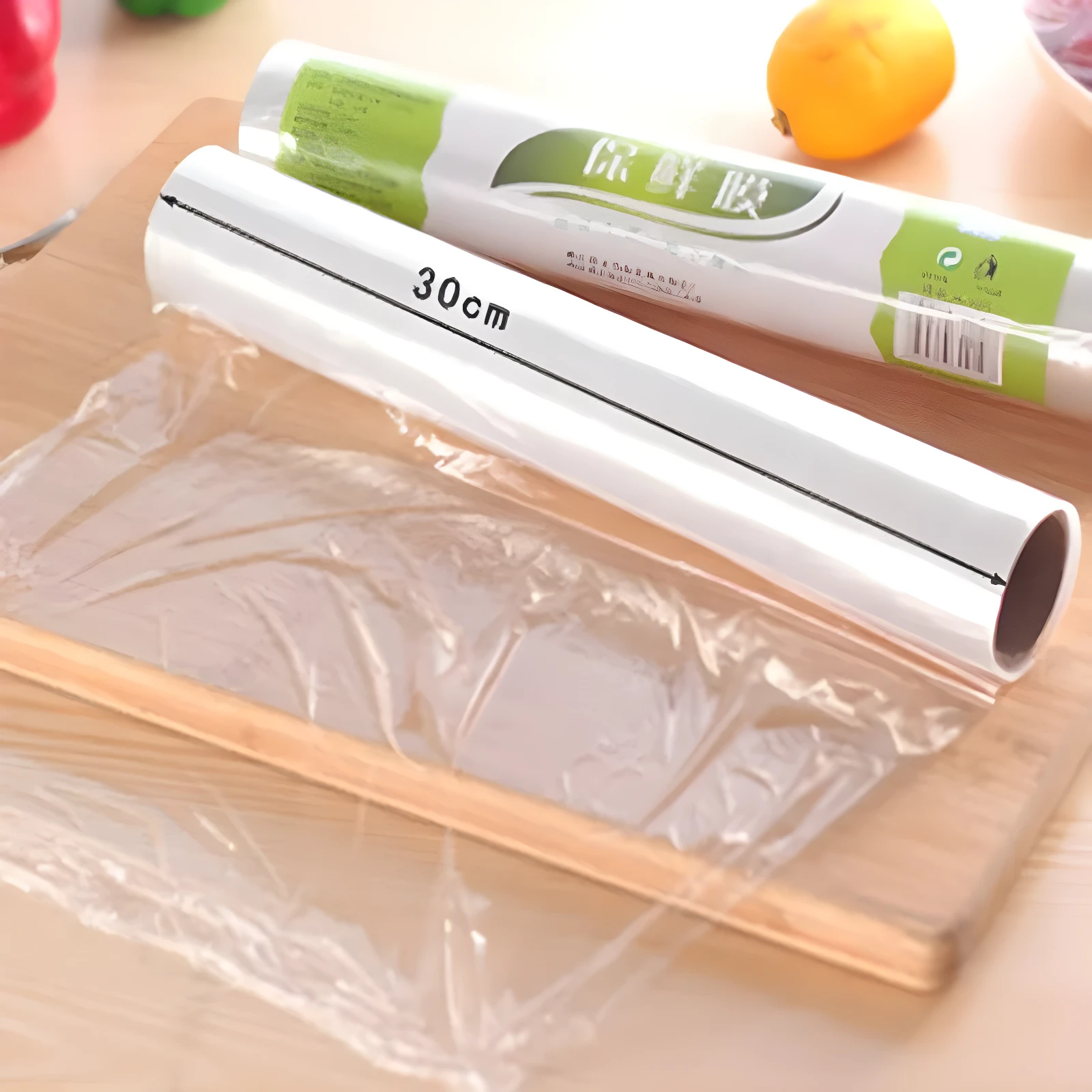 Rollo de película plástica transparente para alimentos, de 30cm de ancho, sobre una tabla de madera con un rollo adicional detrás.