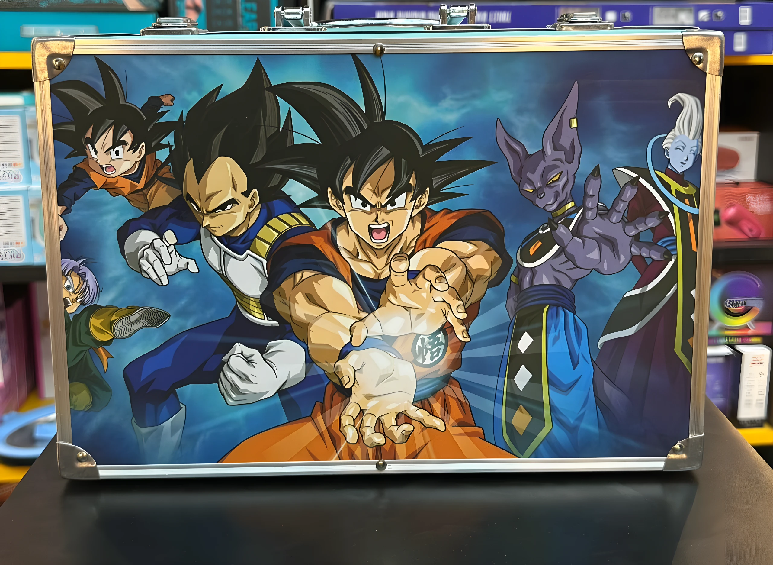 Maletín metálico azul con arte de Dragon Ball Z, Goku, Vegeta, Beerus y Whis.