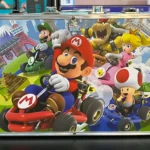 Estuche metálico de Mario Kart con Mario, Luigi, Bowser, Peach y Toad, fondo de escenarios icónicos.