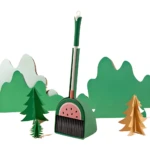 Set de escoba y recogedor verde con diseño de sandía, ambientado con árboles y montañas de papel.