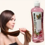 Botella de shampoo rosa con etiqueta que muestra cebolla roja y biotina, junto a mujer de cabello castaño.