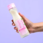 Botella de shampoo Milagros Magia Capilar con tapa rosa, sostenida en mano. Contenido líquido blanco, 400 ml.