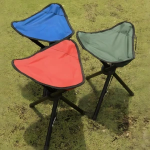 Tres sillas plegables de camping trípodes, asientos rojo, azul y verde oliva, sobre césped verde.