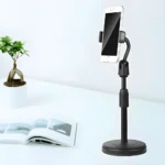 Soporte ajustable para celular en escritorio, negro, ideal para videollamadas y ver contenido, con planta y libro.