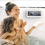 Mujer y niña ríen en bañera con soporte adhesivo impermeable para celular con pantalla encendida.