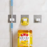 Soporte de pared gris para escoba y botella de aceite de maíz.