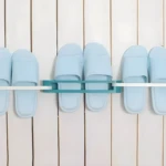 Soporte adhesivo azul para 2 pares de sandalias en pared blanca.