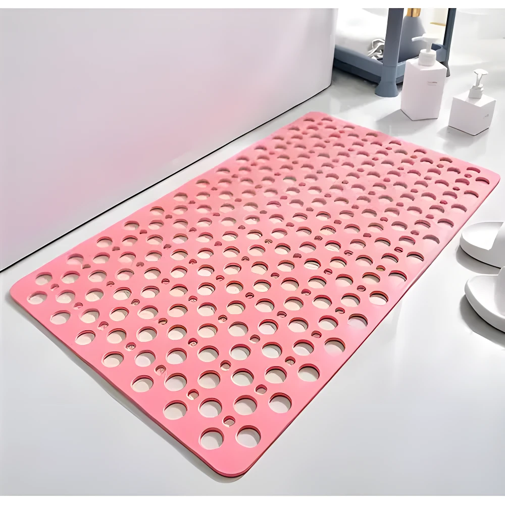 Tapete antideslizante rosa brillante para ducha con múltiples orificios, sobre piso blanco, junto a dispensadores de jabón.