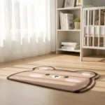 Tapete suave color café claro con diseño de oso durmiendo en cuarto de bebé con cuna blanca y luz natural.
