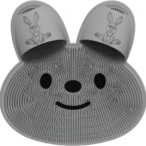 Tapete exfoliante de silicona gris con textura de cerdas, forma de cara de conejo, ranuras para pies y detalles de dibujo de conejo sonriente.