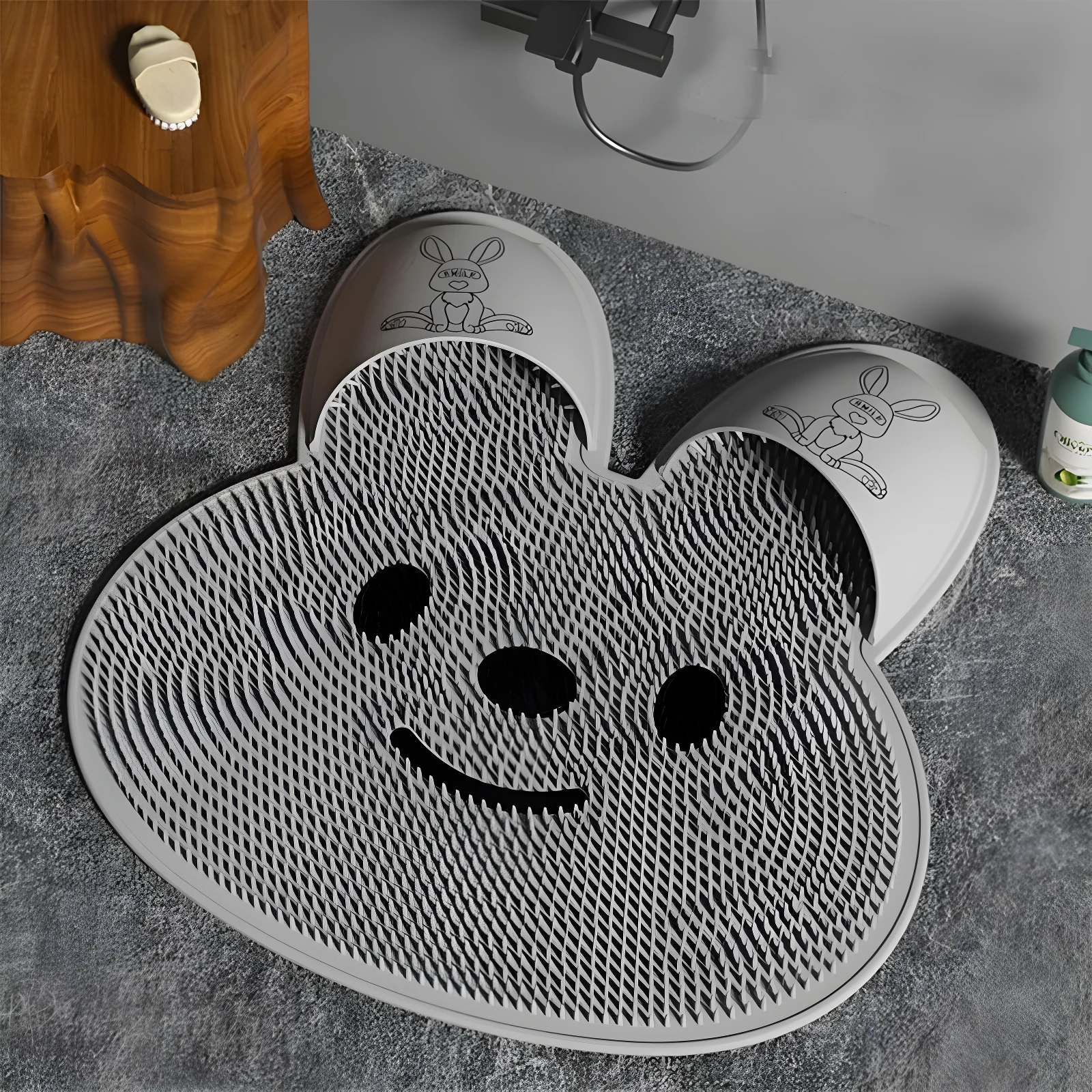 Tapete de baño silicona gris claro con textura exfoliante y diseño de oso sonriente; incluye base para secar pantuflas con estampado de conejo.