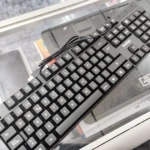 Teclado alámbrico negro Teclop, vista superior, sobre superficie de vidrio con base de enfriamiento visible.