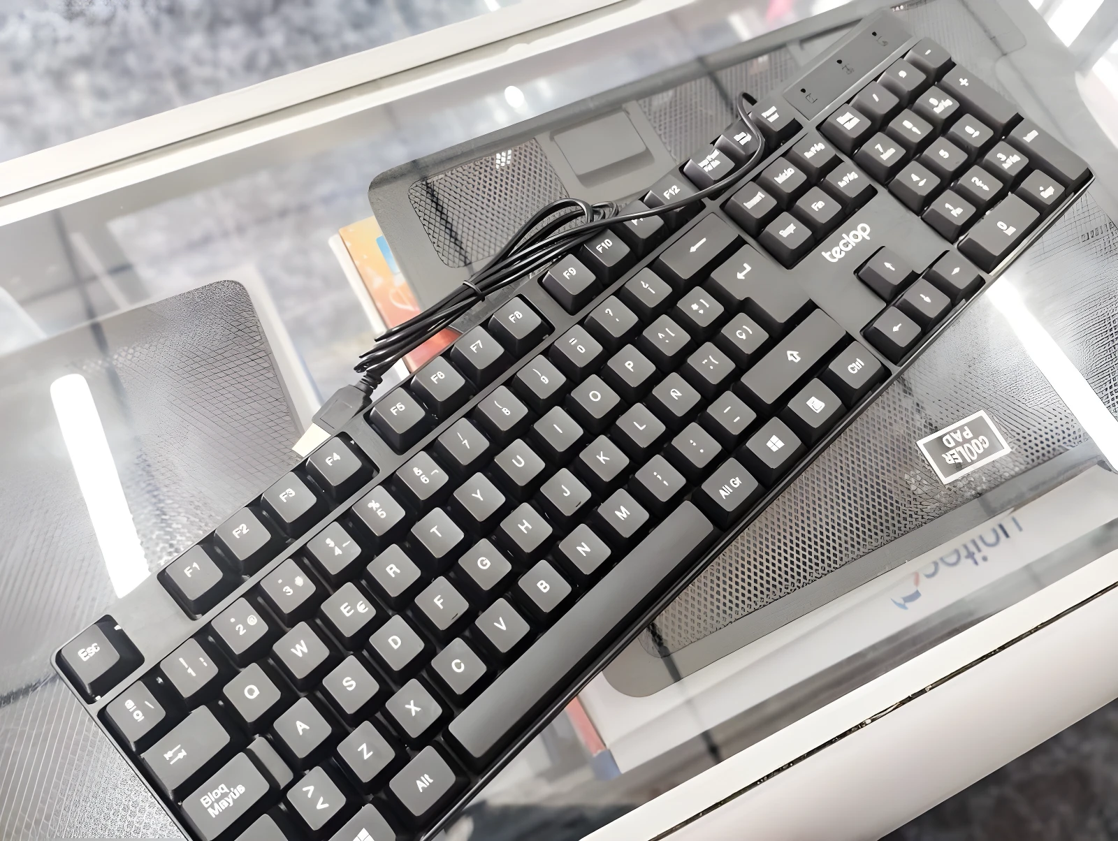 Teclado alámbrico negro Teclop, vista superior, sobre superficie de vidrio con base de enfriamiento visible.