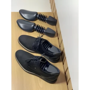 Par de zapatos negros de vestir con hormas para conservarlos, sobre superficie de madera.