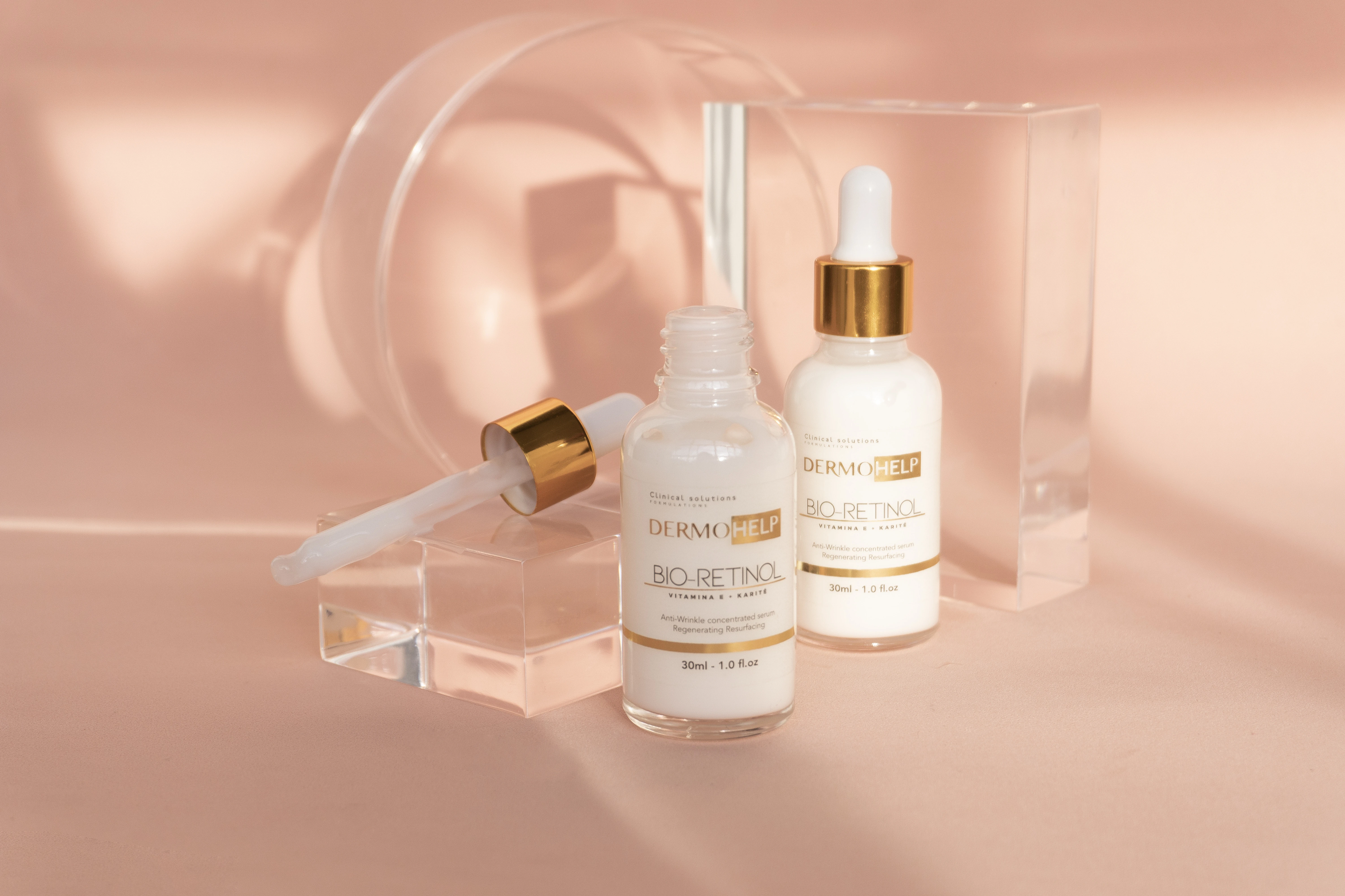 Sérum Bio-Retinol Dermhelp en frasco blanco con aplicador dorado, sobre fondo rosa con luces y texturas.