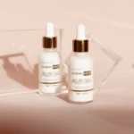 Dos frascos blancos de Sérum Bio-Retinol DermOHELP con gotero dorado, sobre fondo rosa claro, con prismas de cristal.