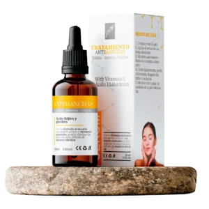 Sérum antimanchas de 30 ml con ácido kójico, glicólico, vitamina C y ácido hialurónico, presentado en frasco ámbar con caja sobre una base de piedra.