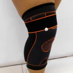Rodillera deportiva de compresión negra con detalles naranjas, para entrenamiento.