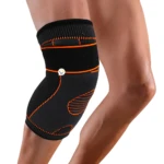 Rodillera deportiva negra con detalles naranja para soporte y compresión, vista en rodilla.