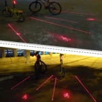 Luces traseras para bicicleta proyectan siluetas rojas de ciclista en el asfalto.