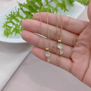 Collar de oro con dije de llave corazón y circonitas, sujetado por una mano.