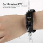 Pulsera inteligente negra sumergible IP67 mostrando hora, fecha y 90% de batería con agua cayendo sobre ella.