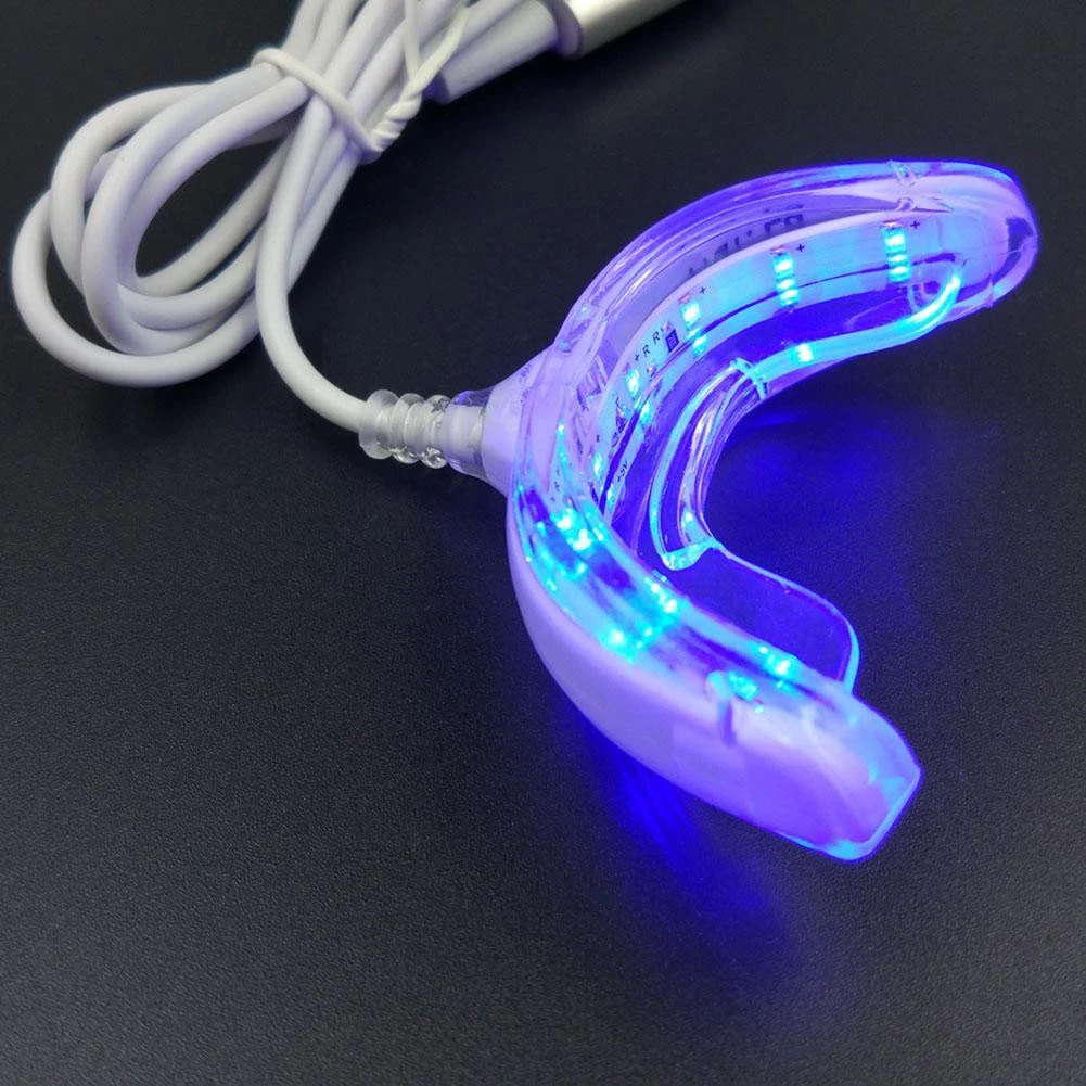 Dispositivo Luxsmile de blanqueamiento dental con luz LED azul encendida, molde bucal transparente de silicona y cable con conector integrado.