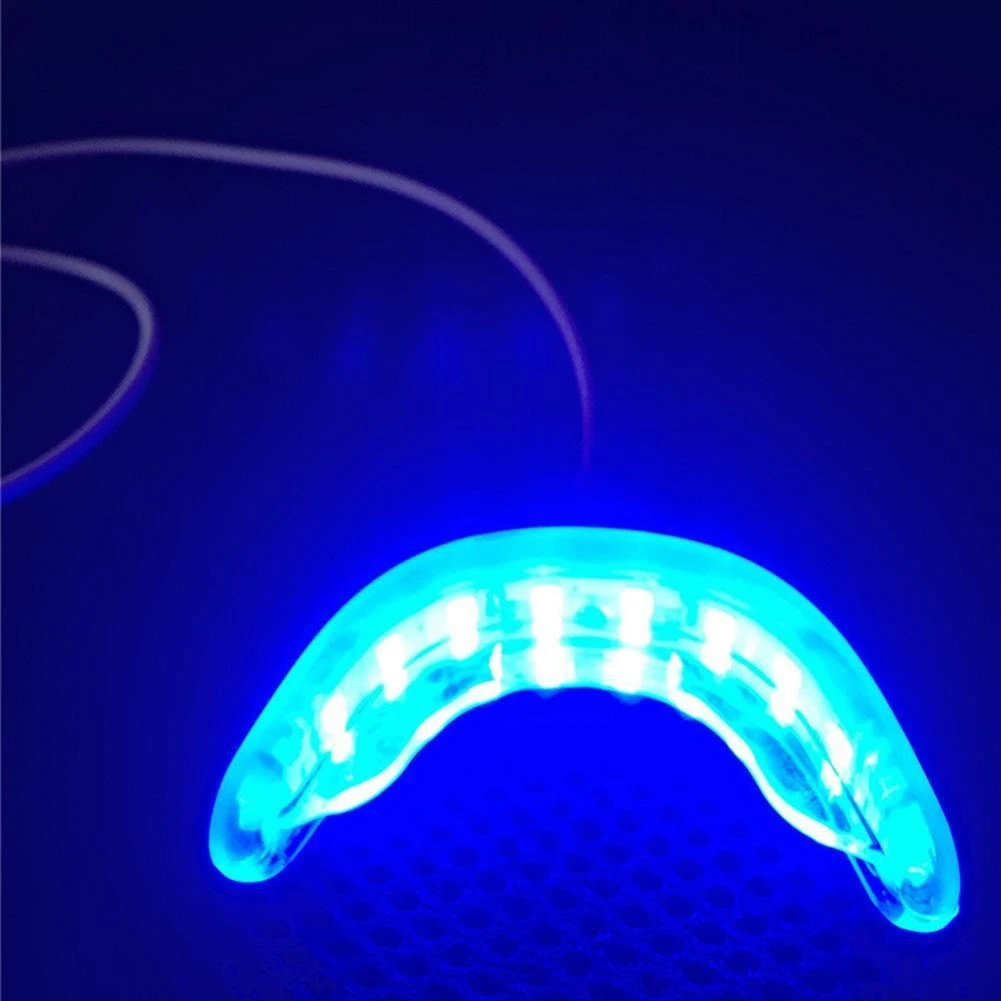 Dispositivo de blanqueamiento dental Luxsmile con luces LED azules encendidas, diseño en forma de arco translúcido y cable de conexión integrado.