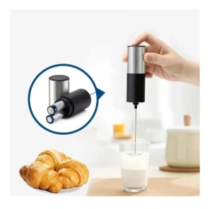Batidor eléctrico portátil plateado y negro mezclando leche en vaso, con croissantes y baterías AAA.