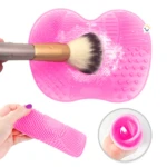 Estera rosa texturizada para limpiar brochas de maquillaje con brocha en uso y accesorio rodante.