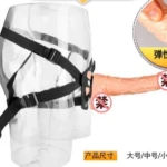 Arnés negro con correas para piernas, sujetando un dildo de silicona texturizada color piel.