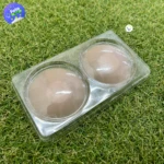 Par de cubre pezones invisibles de silicona color piel, presentados en un blíster plástico transparente sobre una superficie de pasto sintético.