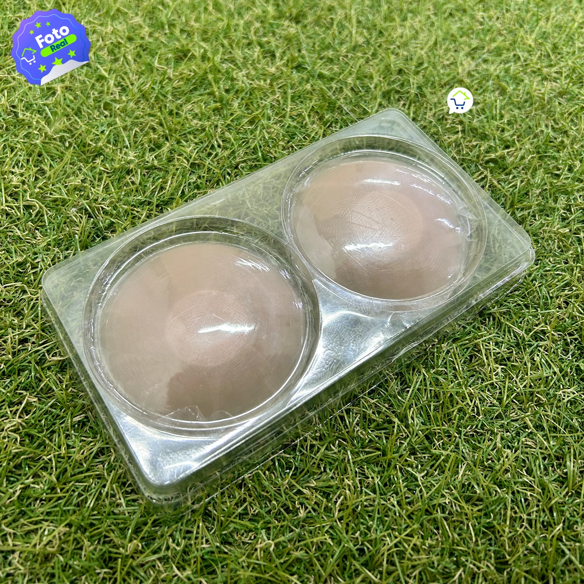 Par de cubre pezones invisibles de silicona color piel, presentados en un blíster plástico transparente sobre una superficie de pasto sintético.