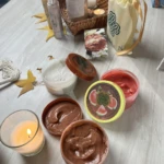 Set de exfoliantes por LERIAN en Cocoa y Sandia, acompañado de velas, jabones y botellas, sobre mesa de madera.