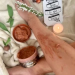 Set de 2 exfoliantes corporales de Cocoa aplicados en la pierna, rodeado de elementos de spa y dulce.