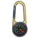 Brújula dorada con mosquetón, ideal para camping, con detalles de navegación y aguja verde apuntando al noreste.