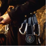Brújula negra con mosquetón para escalada, muestra detallada del dial y accesorios.