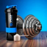 Termo mezclador Spider Bottle negro y azul con pesa y scoop de proteína en tarima de madera.