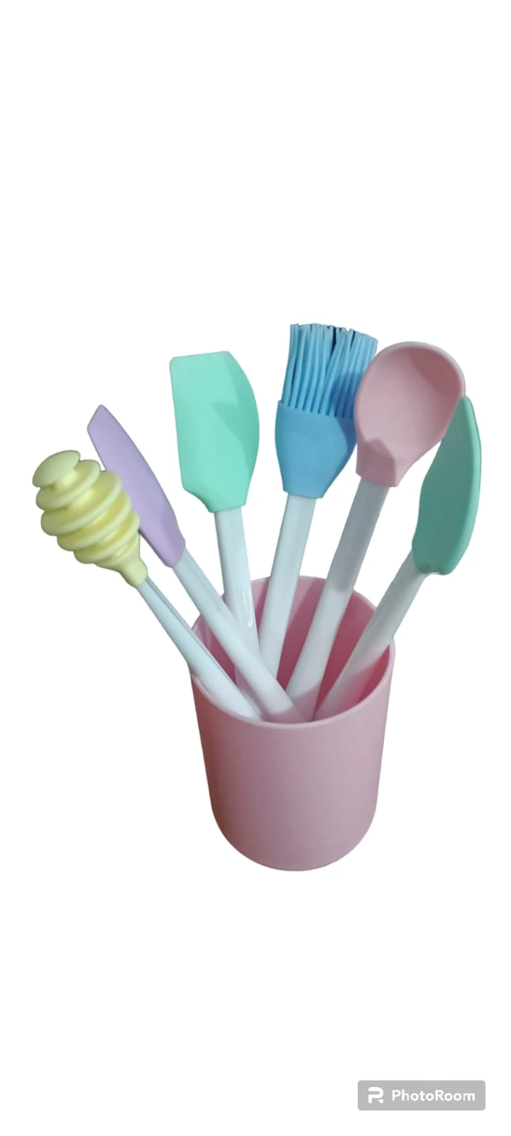Kit de utensilios de cocina en silicona con mango blanco, incluye espátulas, cuchara, brocha y dispersor de miel en tonos pastel dentro de vaso rosa.