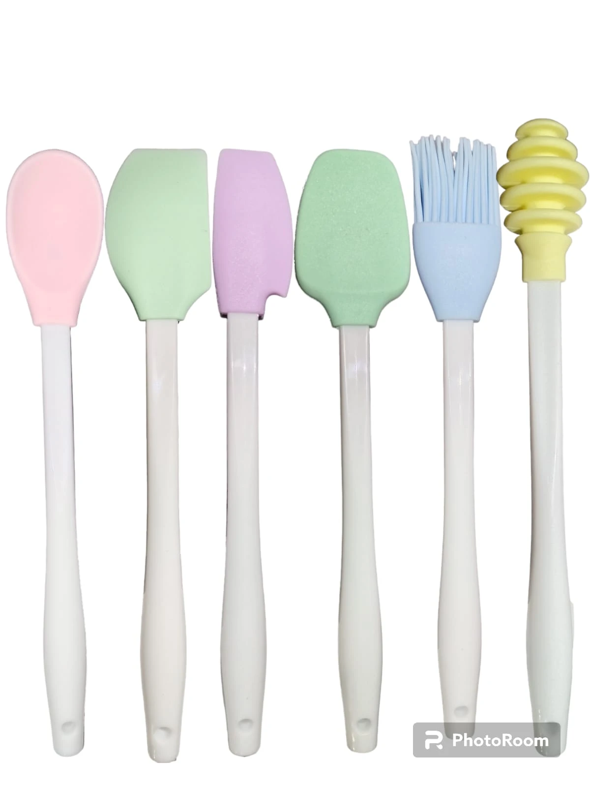 Kit de 6 utensilios de cocina en silicona con mango blanco, incluye espátulas de colores, brocha azul y dispensador de miel amarillo, dispuestos en fila.