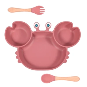 Vajilla adherente rosa con forma de cangrejo, incluye plato con divisiones y cubiertos de silicona con mango de madera.