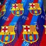 Cobija deportiva FCB azul y roja con logo repetido, textura suave.