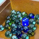 Set de dados y canicas de vidrio de colores azul, verde y transparente en caja de madera.
