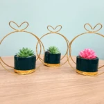 Trío de suculentas artificiales en macetas verde oscuro con soporte dorado, ideal para decorar.